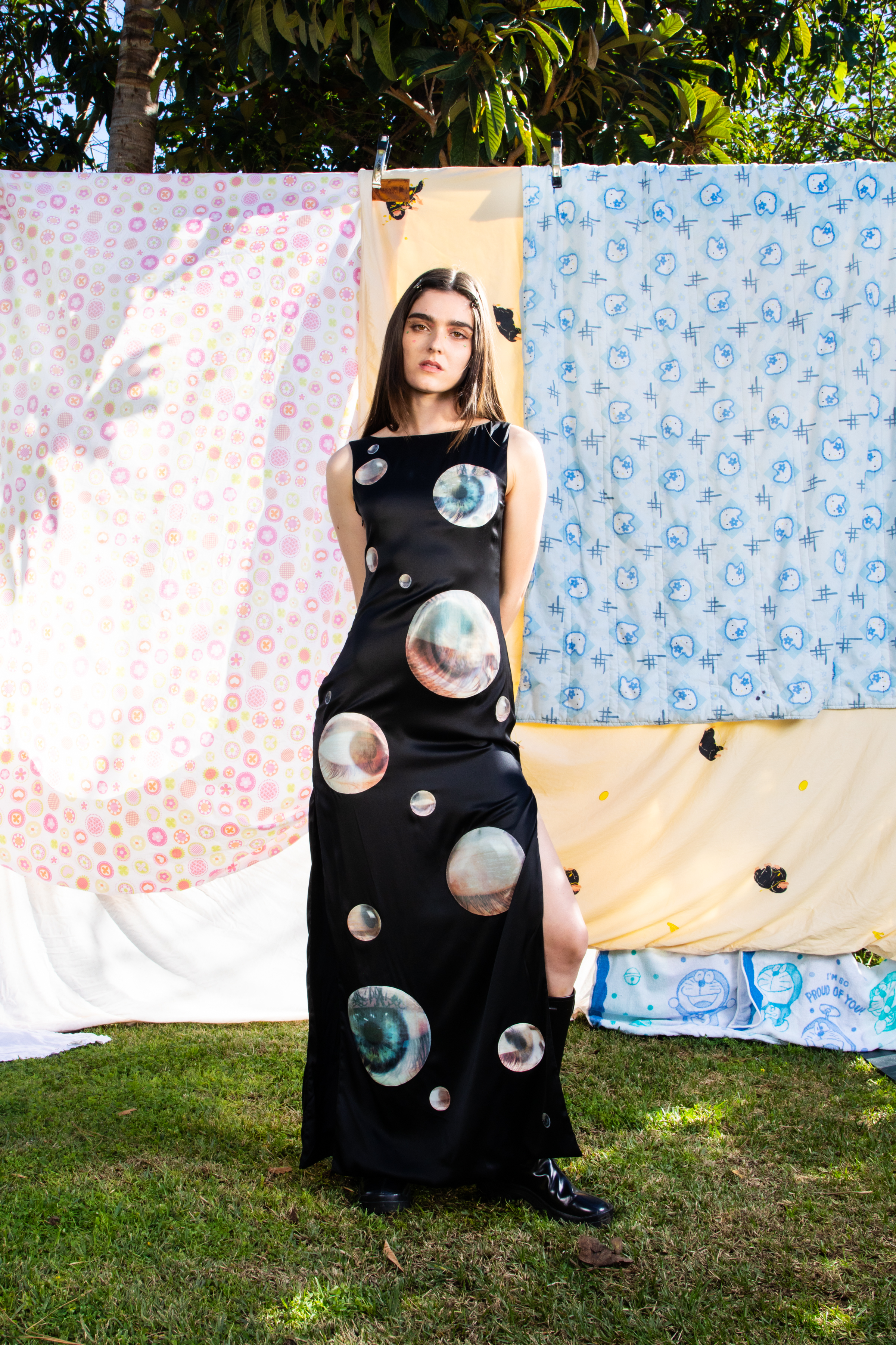 Full body image of a female model wearing a floor legnth patterned black dress against a backdrop of patterned quilts.